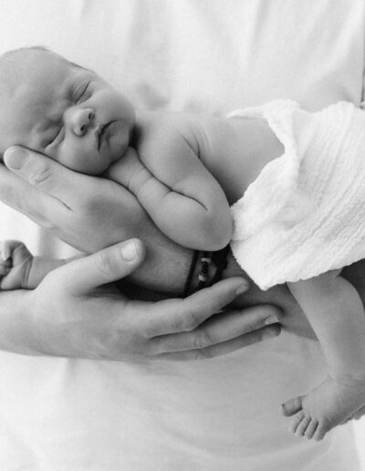 Persönliches Neugeborenen-Shooting: Ein zartes Baby, sicher und geborgen im Arm der Eltern.